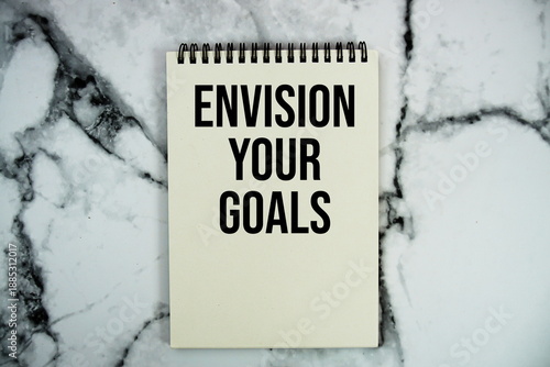 Envision Your Goals text written on notepad flat lay on marble background
