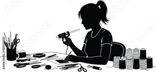 Silhouette of a young woman crafting at a desk using a glue gun surrounded by various handmade hobby tools