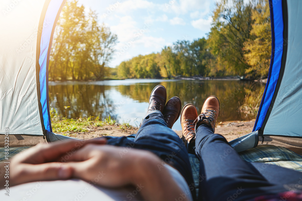 Fototapeta premium Couple, legs and tent by lake for camping, morning and shoes or boots with view in nature. Man, woman and relax in woods for camp, adventure and outdoor together for vacation, holiday and travel