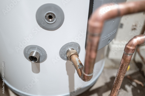 Shallow focus of inlet and outlet flow connections on a newly installed hot water tank in a private home. Copper pipes are being installed.
