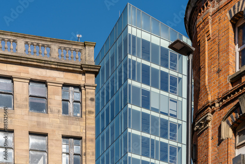 Modern glass office building between historic brick facades in Manchester, England, UK