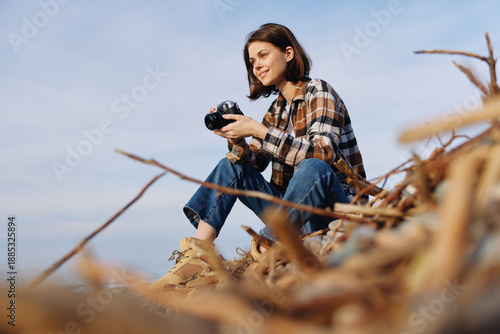 Woman photographer crouches among coastal dunes with a camera, capturing nature, landscape scenes, and bright daylight for an evocative outdoor shot