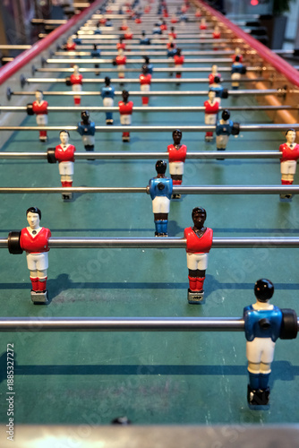 Extra long foosball table designed for group play, featuring red and blue teams on a green soccer-style field indoors.