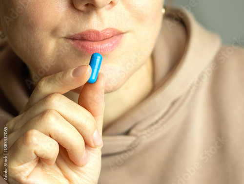 Close-up of a middle-aged woman taking a blue capsule containing dietary supplements or vitamins