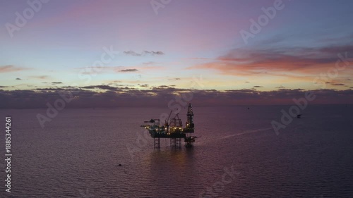 Aerial view from a drone of big jack up offshore drilling oil rig, production platform and supply vessel In the ocean during sunset - Oil and Gas Industry
