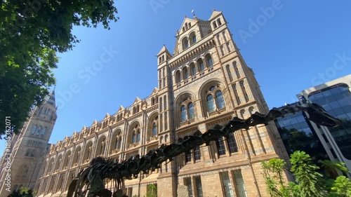 Wide view of the Natural History Museum exterior surrounded by greenery under a clear blue sky in London, UK