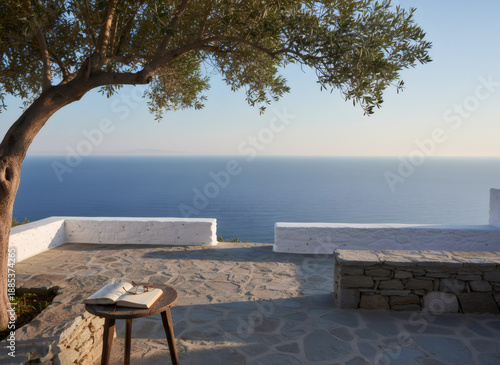 Outdoor patio overlooking the sea with an olive tree, book, and glasses on a small wood table. Mediterranean landscape for travel, vacation.
