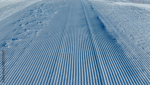 Perfectly groomed ski piste with smooth corduroy snow leading toward alpine slopes, designed for winter sports, resort branding, and seasonal outdoor concepts