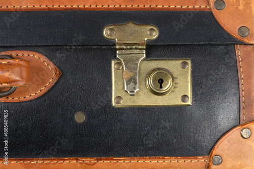A close-up shot captures the tarnished brass lock mechanism on a vintage black suitcase with contrasting brown leather trim and stitching