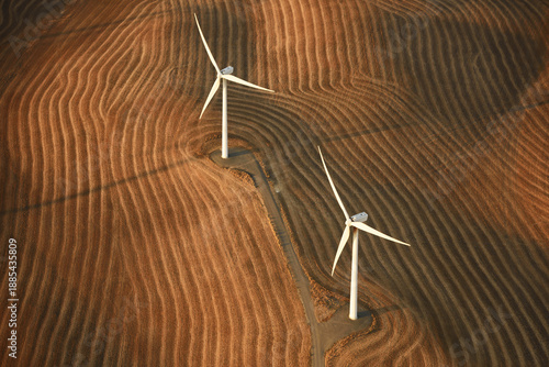 Aerial view of two wind turbines casting long shadows over the rippled, golden fields, creating a striking contrast of light and shadow, Washtucna, Washington, United States.