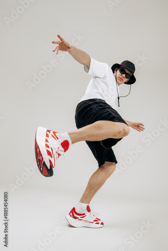 Full body shot of a stylish male dancer performing dynamic moves. Low angle wide-angle perspective emphasizes motion, energy and modern street dance style in studio.