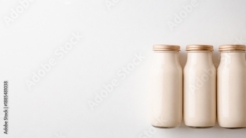 Three glass bottles with pale beige liquid stand on a pale background creating a simple, balanced composition