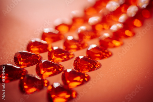 Close-up view of shiny, red heart-shaped gemstones arranged in vertical rows on a coral background, with shallow depth of field and soft focus.