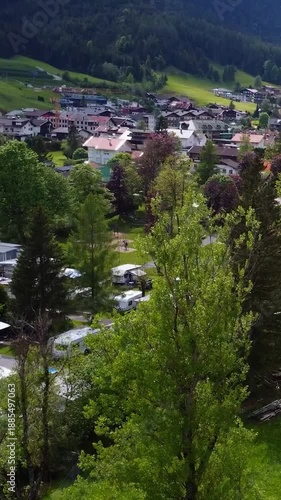 Aerial view of a scenic alpine village with a riverside campsite and traditional houses in Tyrol, Austria.