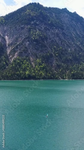 Aerial view of a winding road along the turquoise Lake Plansee in the Tyrolean Alps, Austria.