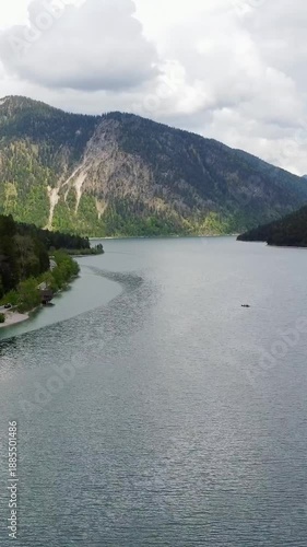 Aerial view of a car driving on a scenic winding road along Lake Plansee in the Austrian Alps.