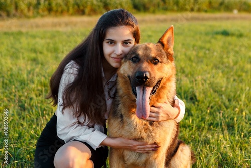 Young woman is kneeling and embracing a german shepherd dog in a vibrant green field, creating a heartwarming scene of companionship and love between human and animal