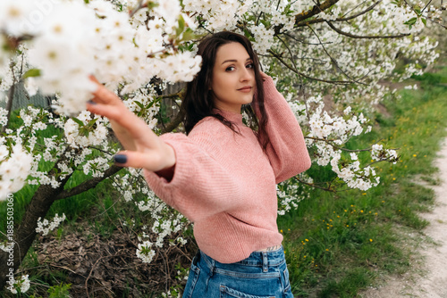 Fashionable young woman gently touching cherry blossoms while posing in a blooming spring orchard, enjoying the beauty of nature and the pleasant weather