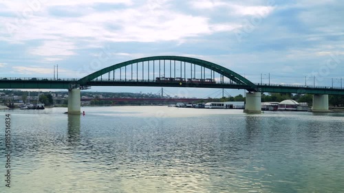 Trolleys and other traffic crossing old iron bridge above wide river in city, urban landscape, dramatic sky