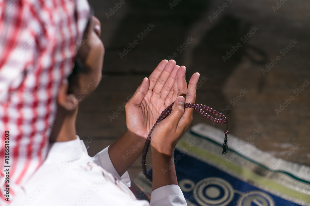 Obraz premium Close-up image of a hand reaching out while holding a prayer bead, a prayer gesture (do'a) of an Asian Muslim man inside the house.