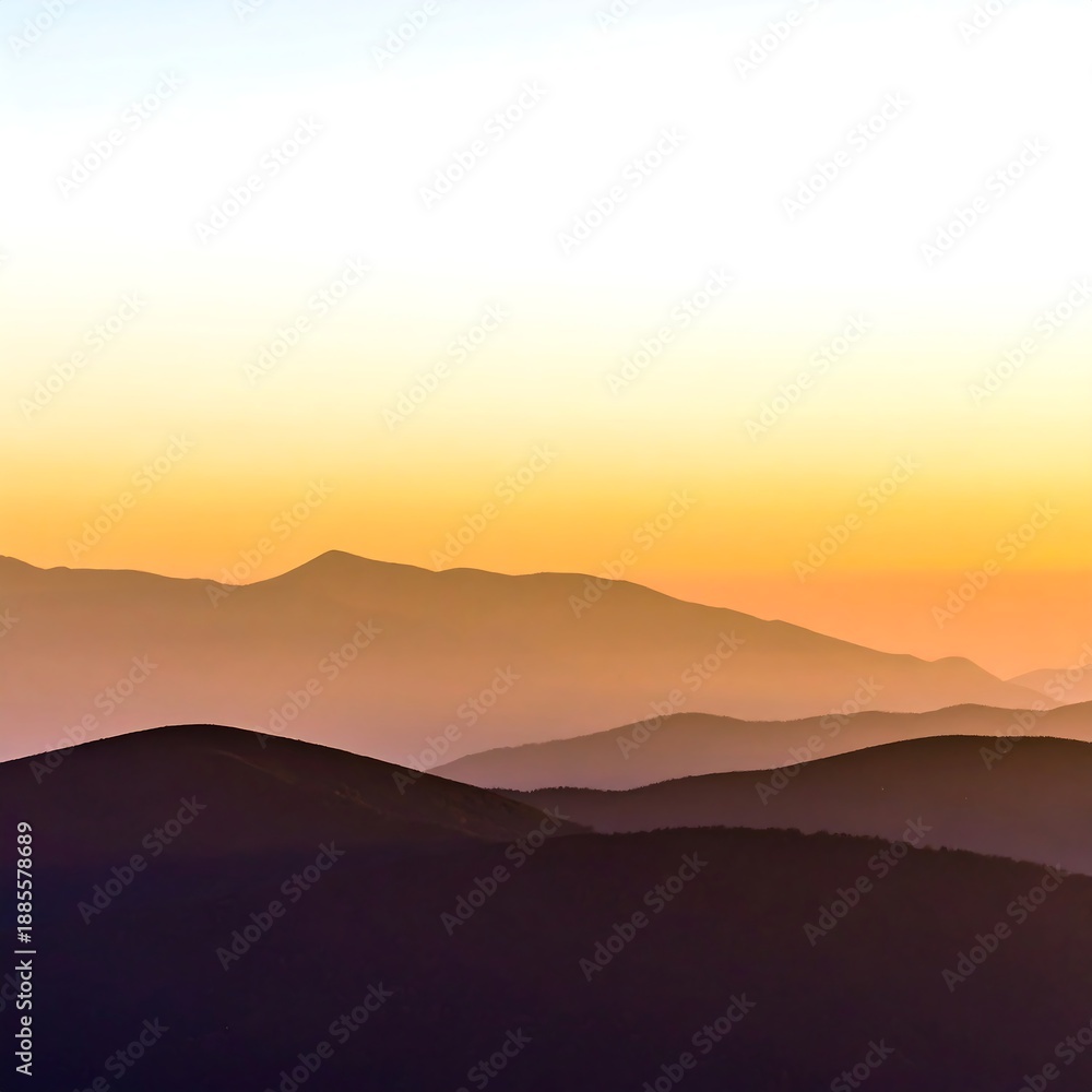 Fototapeta premium Layered mountain silhouettes fade into a warm, colorful sky at sunset or sunrise