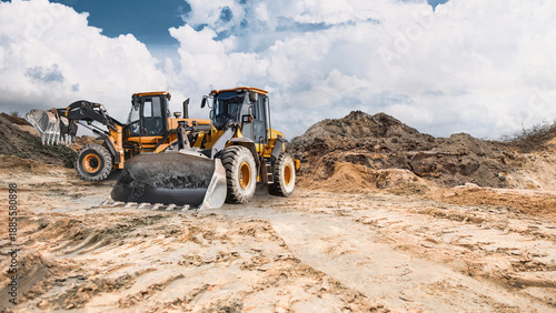 Two powerful wheel loaders stand ready to work in a sand quarry, while clouds disperse across the blue sky. The equipment is ready for construction work