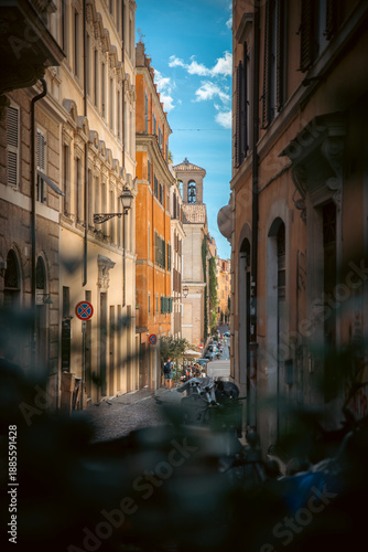 Narrow European street with historic buildings and pedestrians under a bright blue sky. Rome Italy