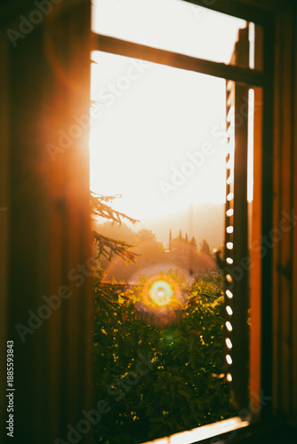 Sunset view from an open window overlooking a lush garden, with warm sunlight streaming in. Italy Tuscany