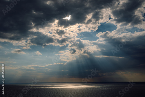 Fotografie A dramatic seascape featuring crepuscular rays (God rays) breaking through a dense canopy of dark, heavy storm clouds