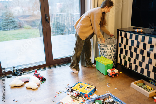 Woman cleans room after her child played, picking up toys and organizing space during afternoon at home
