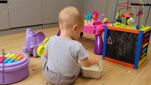 Cute little toddler baby child playing on the floor at home, Mess due to toys scattered on the floor