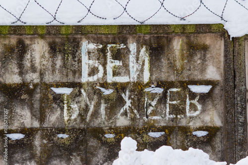 Wallpaper Mural Faded Russian Beat the Bourgeois graffiti on a mossy concrete fence, a post-Soviet era relic. Weathered urban texture with snow and barbed wire, Russia Torontodigital.ca