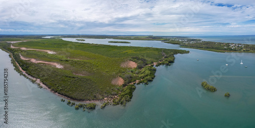Aerial view of the serpentine river snaking through verdant mangroves, meeting the cerulean sea under a cloudy sky, River Heads, Queensland, Australia.