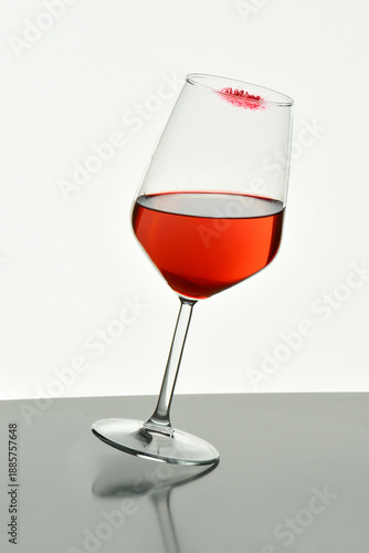 Foto Minimal still life of a tilted wine glass with red beverage on a reflective surface, isolated on white background