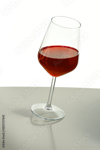 Valokuva Minimal still life of a tilted wine glass with red beverage on a reflective surface, isolated on white background