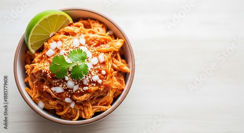 Delicious chicken tinga dish with lime and cilantro in a bowl on a white table