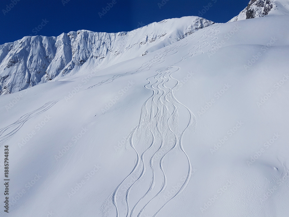 Obraz premium AERIAL: Cool shot of snowboarder and skier trails running down snowy mountain.