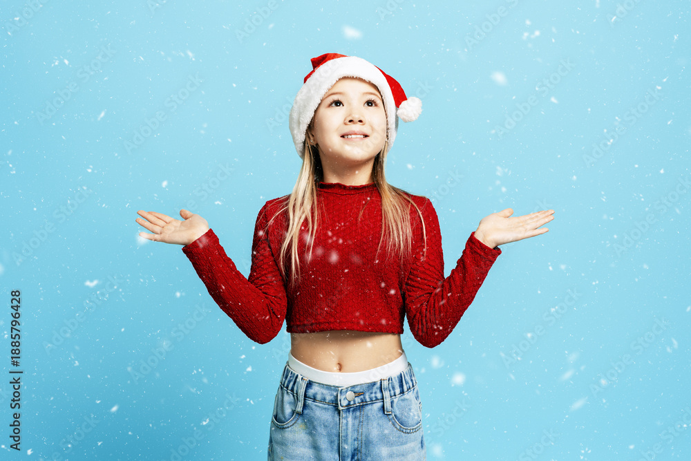 Fototapeta premium Young girl wearing Santa hat catching falling snow for winter holidays