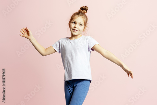 Happy little girl raising hands expressing joy and fun on pink background