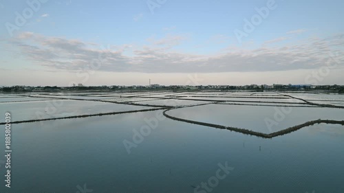 Aerial view of flooded rice paddies in Yilan County, Taiwan, at dusk. The calm water reflects the soft hues of the sky and slowly moving clouds, creating a serene and picturesque rural landscape.