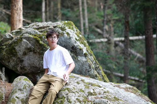 Young man in glasses sitting on mossy rock in forest