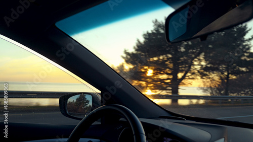 View from inside a car on a scenic road trip at sunset. The warm golden light filters through trees along a coastal highway. First-person perspective creates a calm, nostalgic travel mood. Cinematic