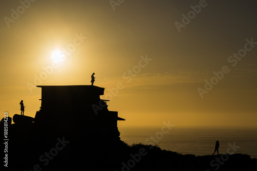 Silhouettes of tourists watching the sunset over the Atlantic Ocean in Galicia, Spain. Golden hour at a coastal viewpoint