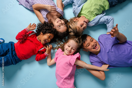 Portrait of happy multinational children laughing lying in circle looking at camera fooling around