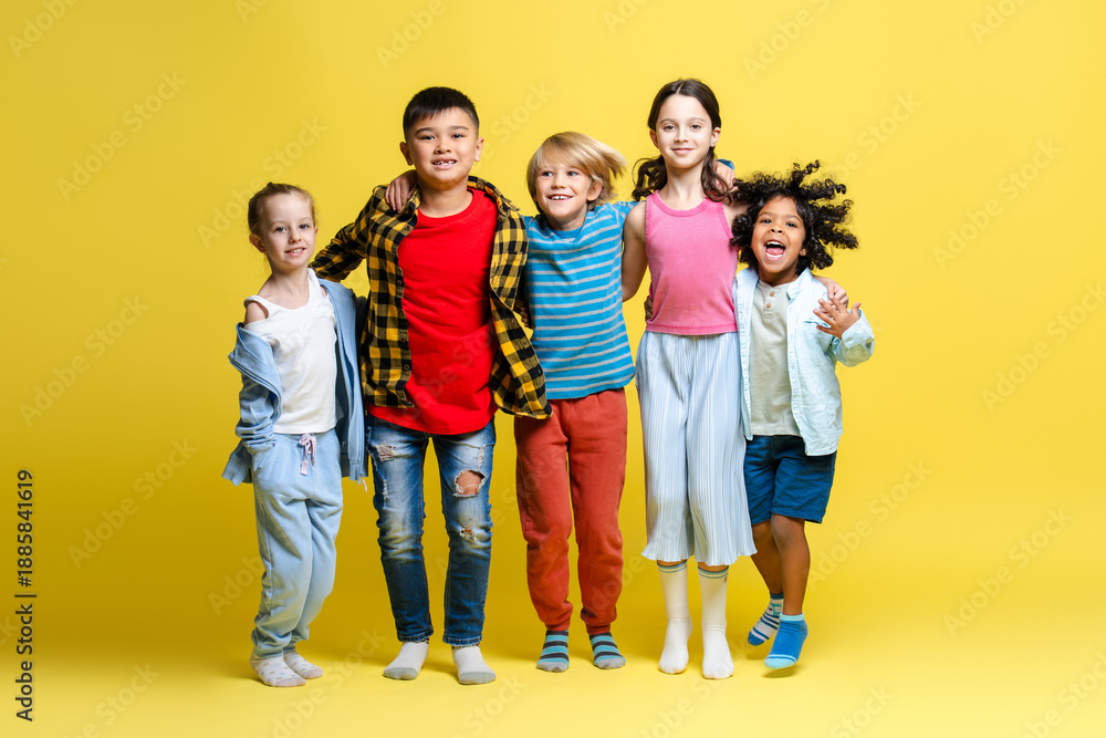 Obraz premium Group of happy multinational kids, happy boys and girls hugging together on yellow background