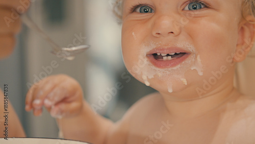 Tableau sur toile Close-up of a happy blue-eyed baby messy face while being fed porridge