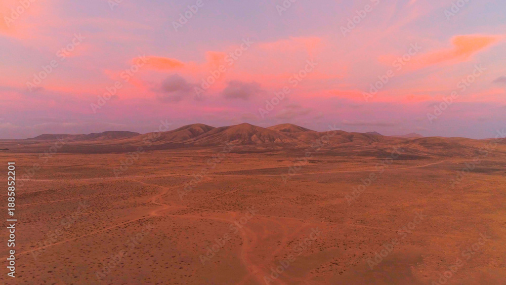 Fototapeta premium AERIAL: Flying away from big volcanic structure in pink colored desert sunset.