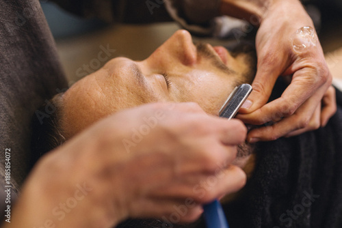 Tableau sur toile Close up of professional barber shaving male neck with straight razor in barbershop