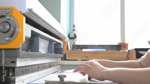 Women's hands in the printing house work at the machine, making holes in the paper to insert the spring for the notebook. Production of calendars and brochures