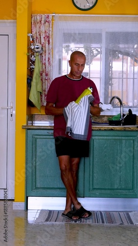 Adult man performing household chores and maintaining his home environment with a dishcloth and cleaning bottle, embodying a routine of tidiness and personal care
